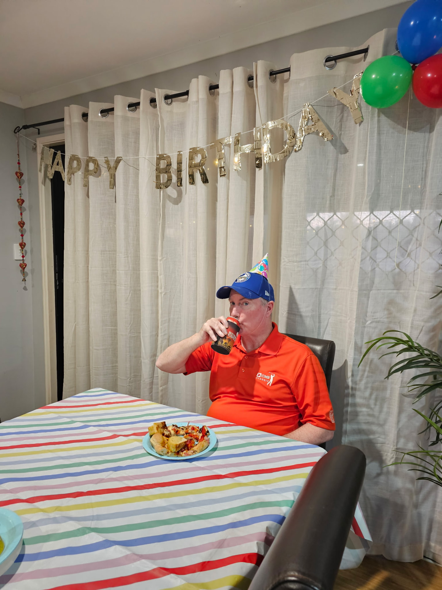 A man enjoying a birthday lunch under a Happy Birthday banner and balloons