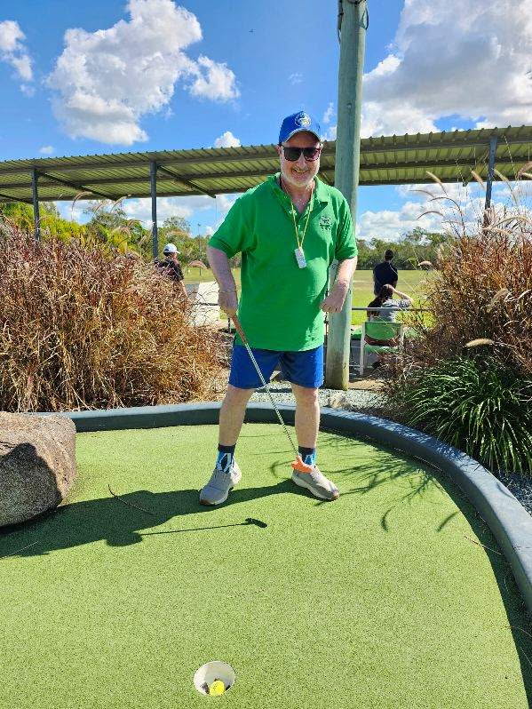 A man in a green polo shirt lining up a putt on a sunny mini golf green