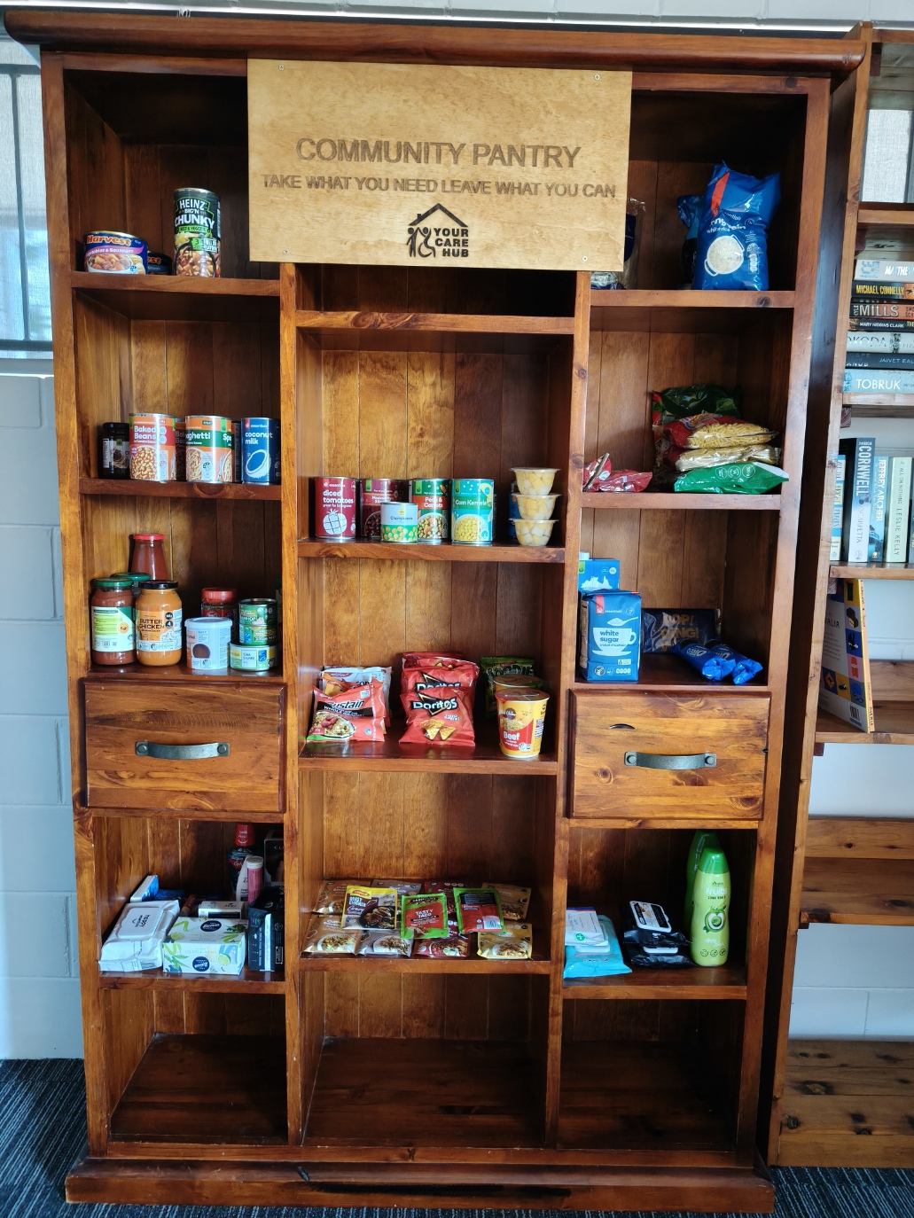 The Community Pantry cabinet stocked with non-perishable food and household essentials at Your Care Hub