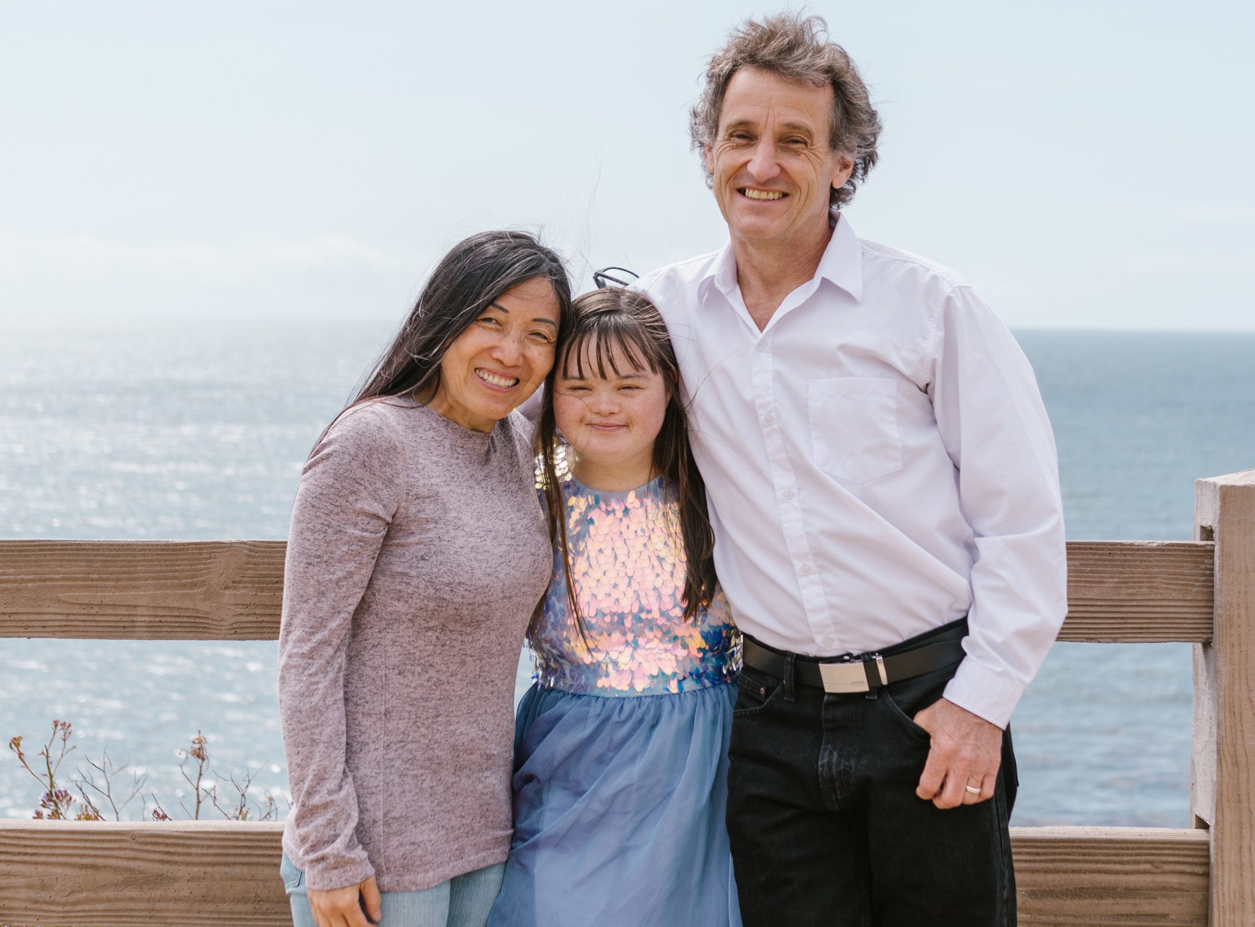 A father and mother standing on either side of their daughter who is an NDIS participant